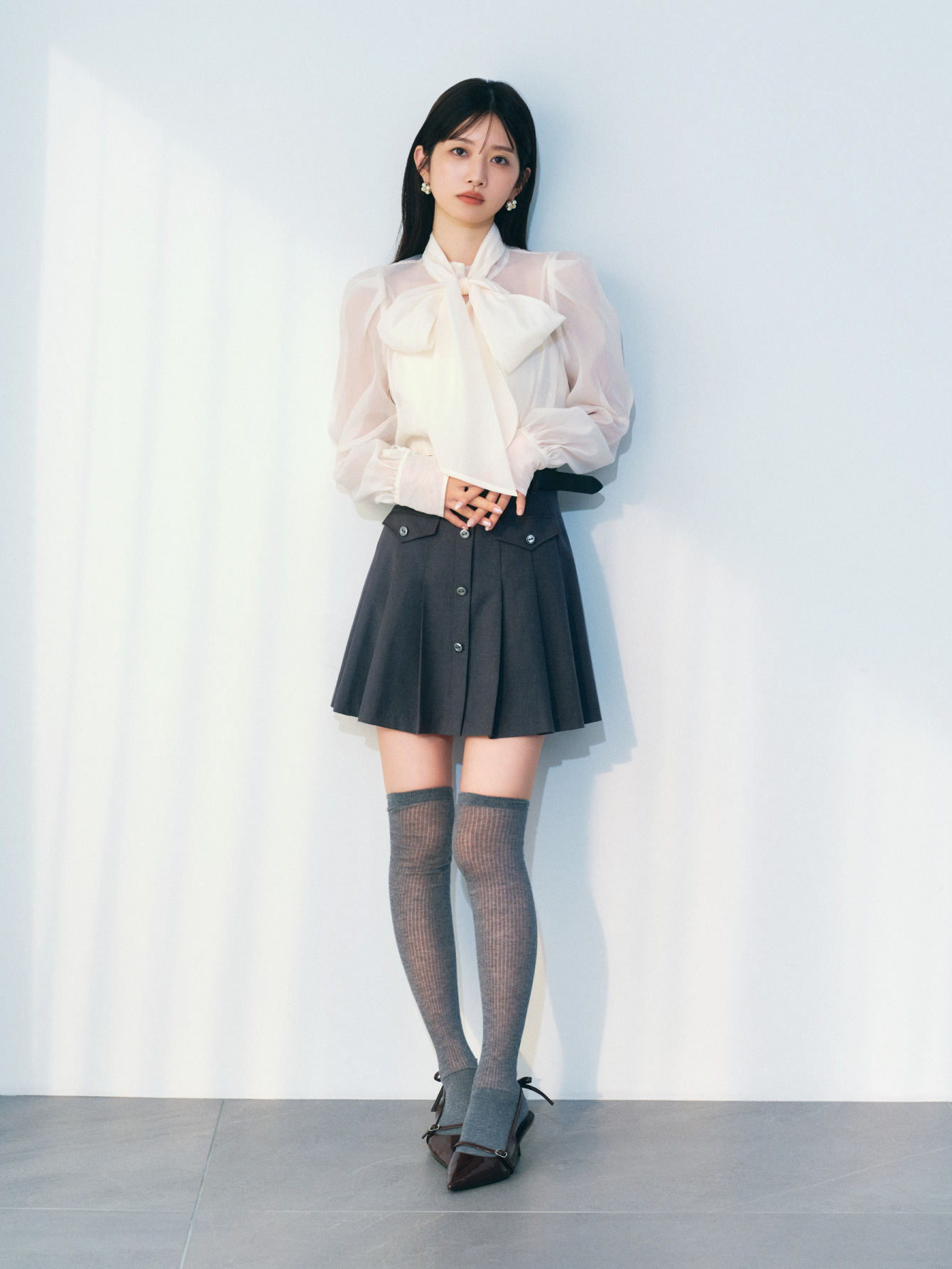 アイボリーのビックボウタイブラウス・グレーのベルト付きプリーツスカショーパンとシアーコットンニーハイソックス・ブラウンのリボンスリングバックパンプス・LBロゴパールピアスの着用例