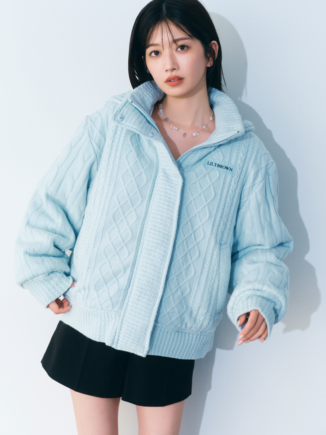 ライトブルーのニットパフジャケット・白のベロアフリルトップス・黒のベルト付きショートパンツ・銀のLilywingビジューフラワーネックレスの着用例