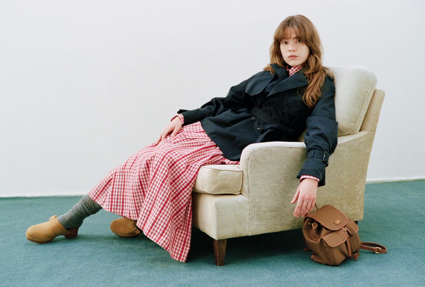 クラシックミドルトレンチコート＆Lily Bearレターモチーフバリエシャツ＆２wayボリュームシャツスカート＆2wayバックパック＆ウッドソールスタッズサボを着用した女性