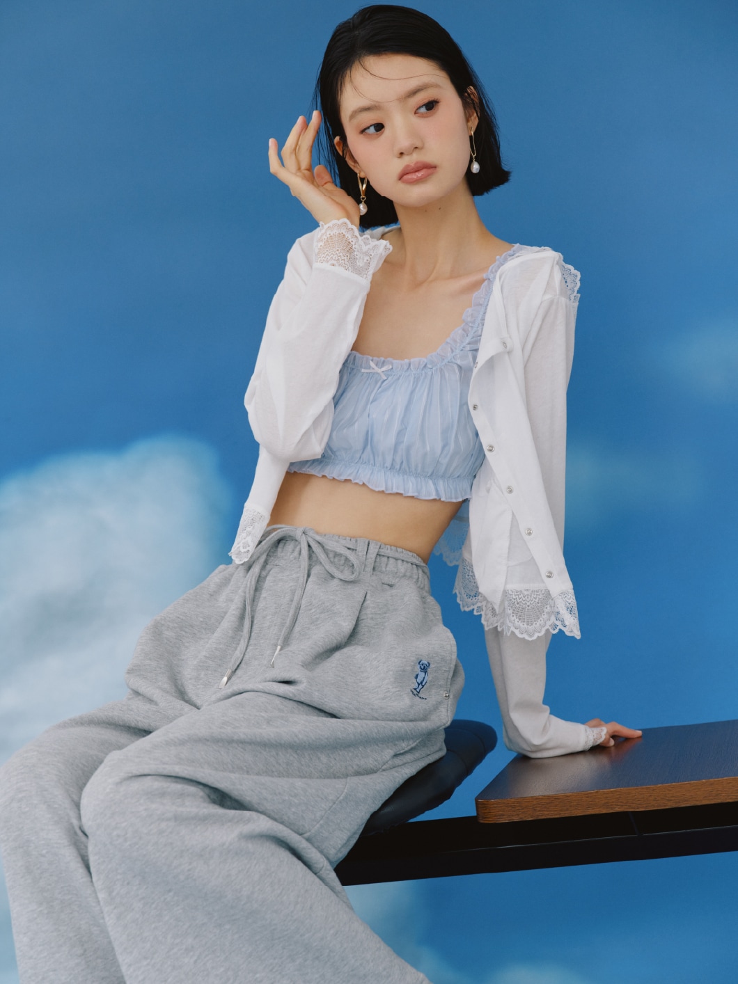 白のレースフーディトップス・ブルーのシアーストライプシャーリングビスチェ・グレーのスウェットパンツ・ピアス・ラベンダーのシューズを合わせたコーディネート