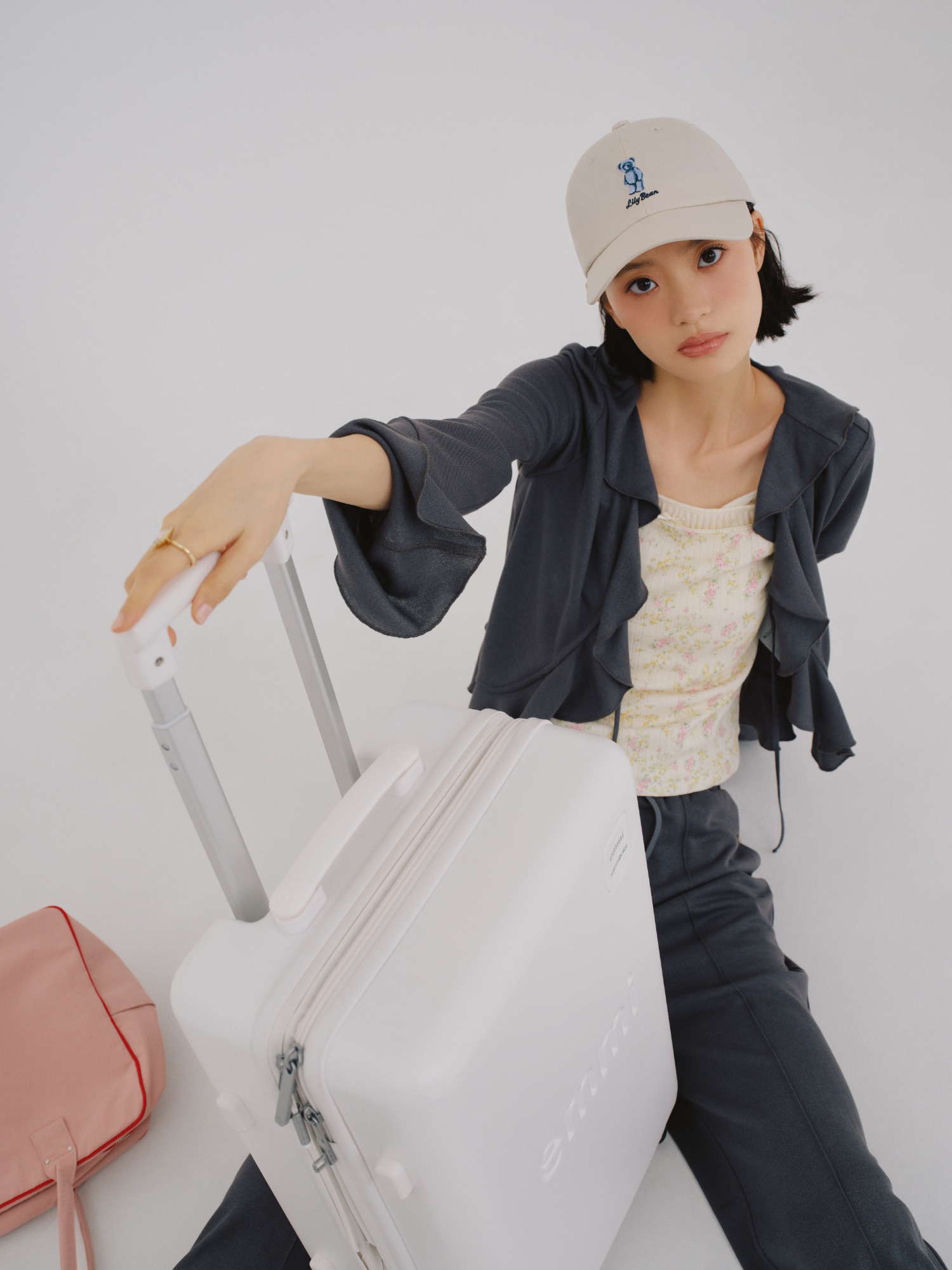 チャコールグレーのフリルカットカーディガンとカットロングパンツ・イエローのレイヤードキャミソール・ピンクのボストンバッグ・アイボリーのキャップ・リング・オフホワイトのレースアップスリングバッグパンプスを合わせたコーディネート