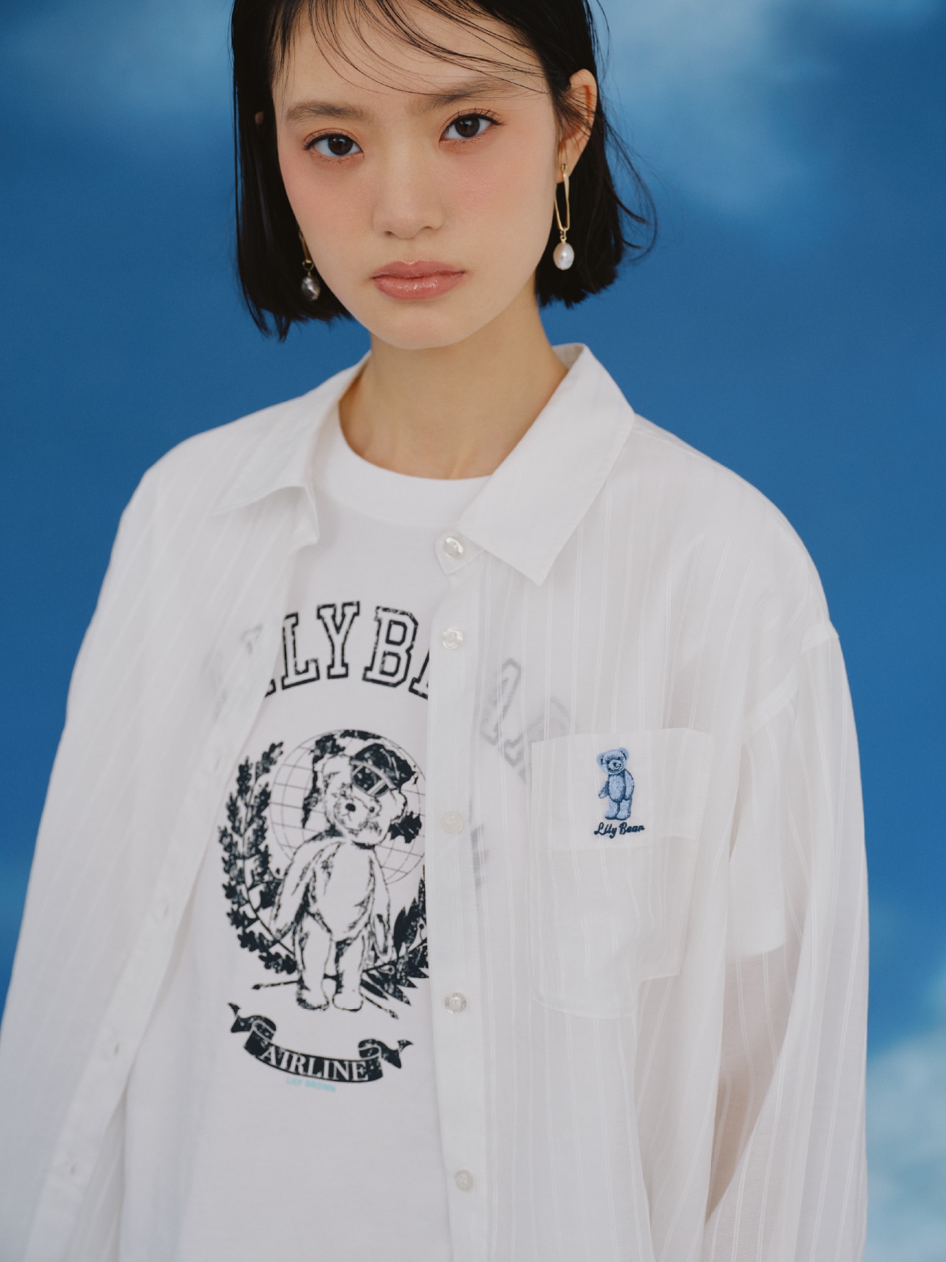 白のシアーシャツとTシャツ・ネイビーのサテンランジェリーショートパンツ・ダークネイビーのボストンバッグ・チャーム・ピアス・黒のレースアップショートブーツを合わせたコーディネート