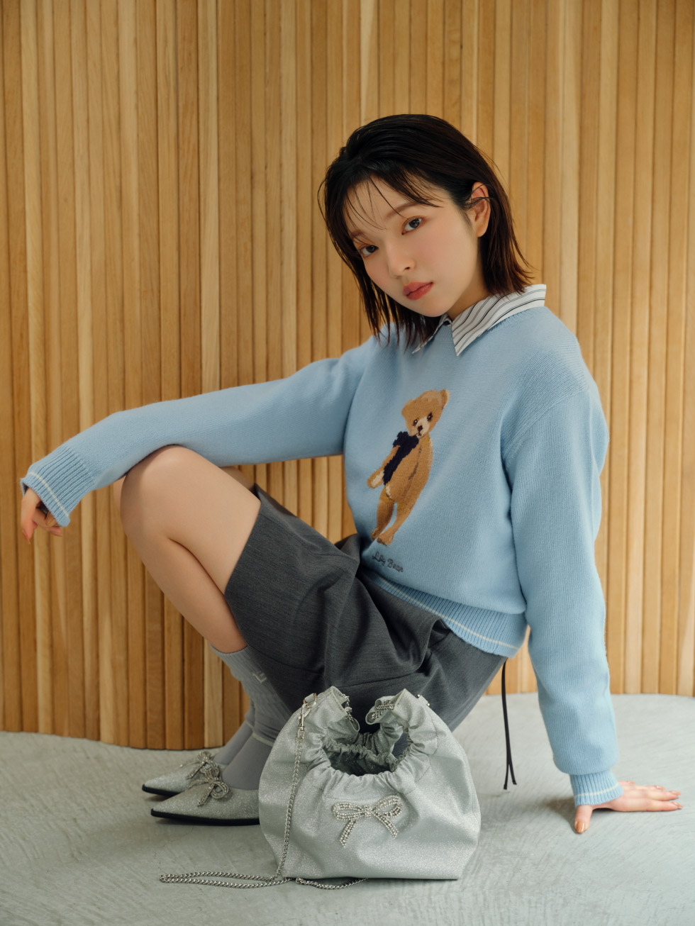 コクーンフレアミニスカート・タイ付きクロップドシャツ・【WEB限定カラー】Lily Bearリボンニットプルオーバー・[L.B CANDY STOCK]ビジューミュール・[L.B CANDY STOCK]ビジューワンハンドルバッグ・モノグラムソックスを着用した女性