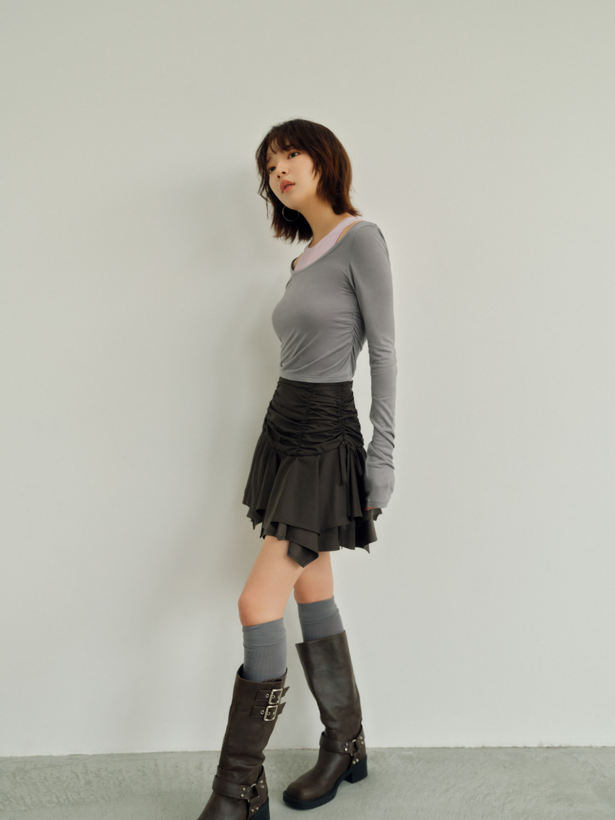 ランダムヘムギャザーミニスカート・レイヤードセットカットソー・バイカーブーツ・リブニーハイソックスを着用した女性